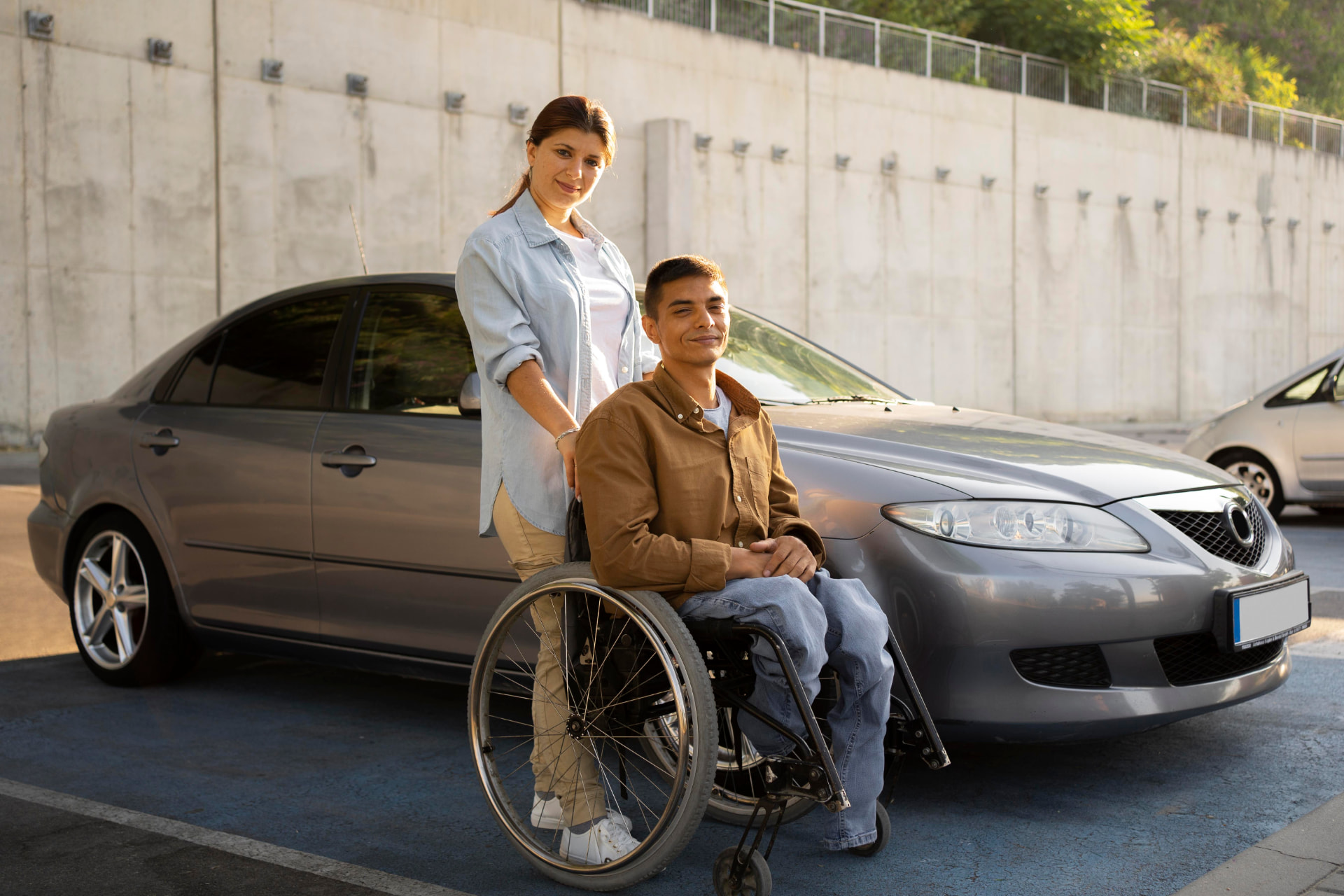 A smiling man in a wheelchair with his support worker beside their car, ready to head out