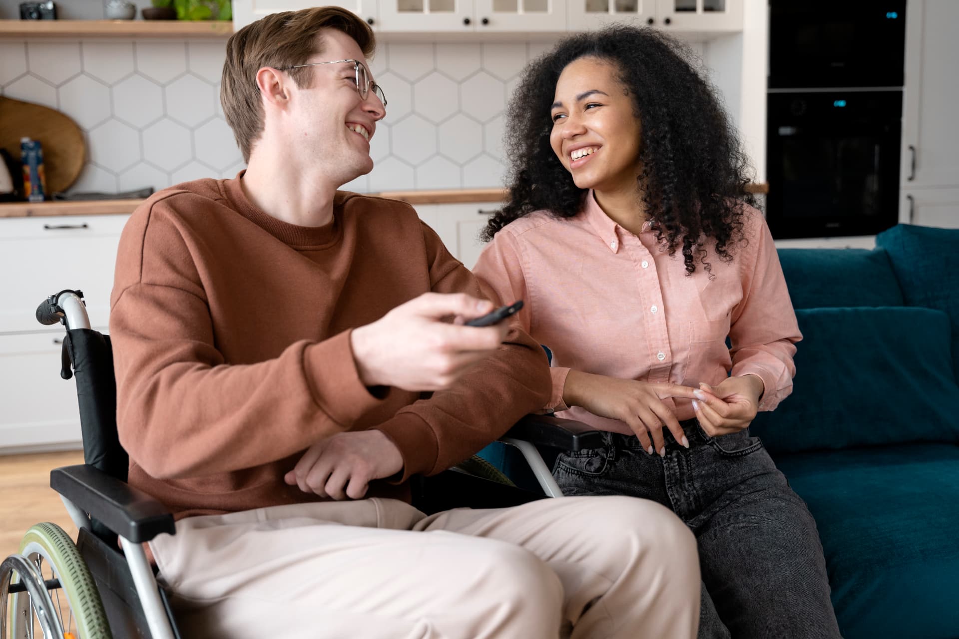 Two friends, one a wheelchair user, laughing together at home